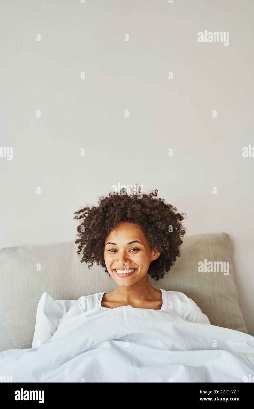 Lockige junge Frau mit einem strahlenden Lächeln, das im Bett ruht Stockfoto