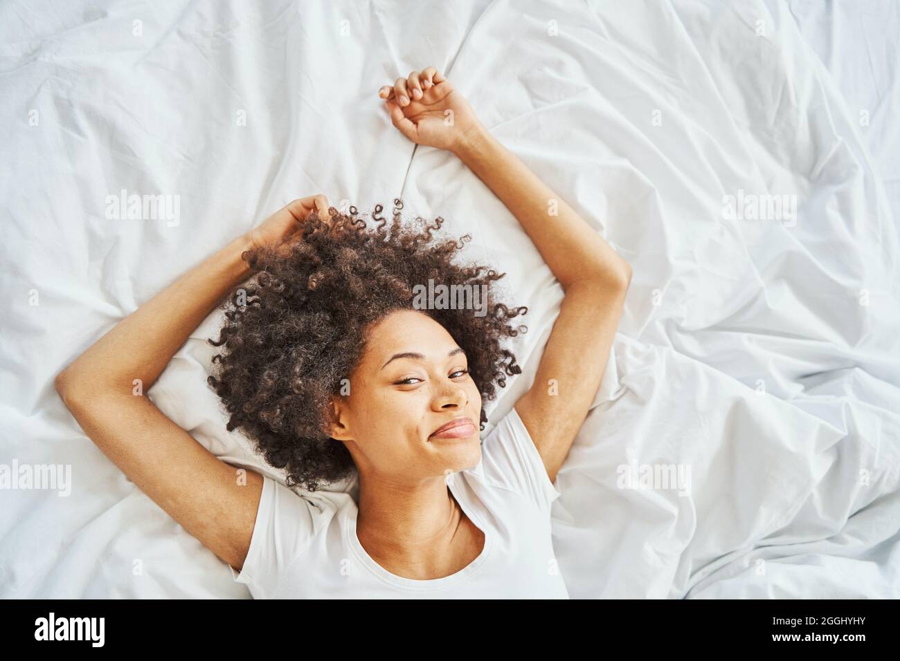 Zufriedene afroamerikanische reizende Frau, die sich im Bett ausruhte Stockfoto