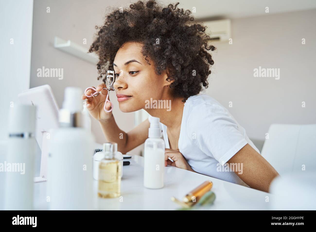 Fokussierte junge Frau mit einem Wimpern-Lockenstab zu Hause Stockfoto