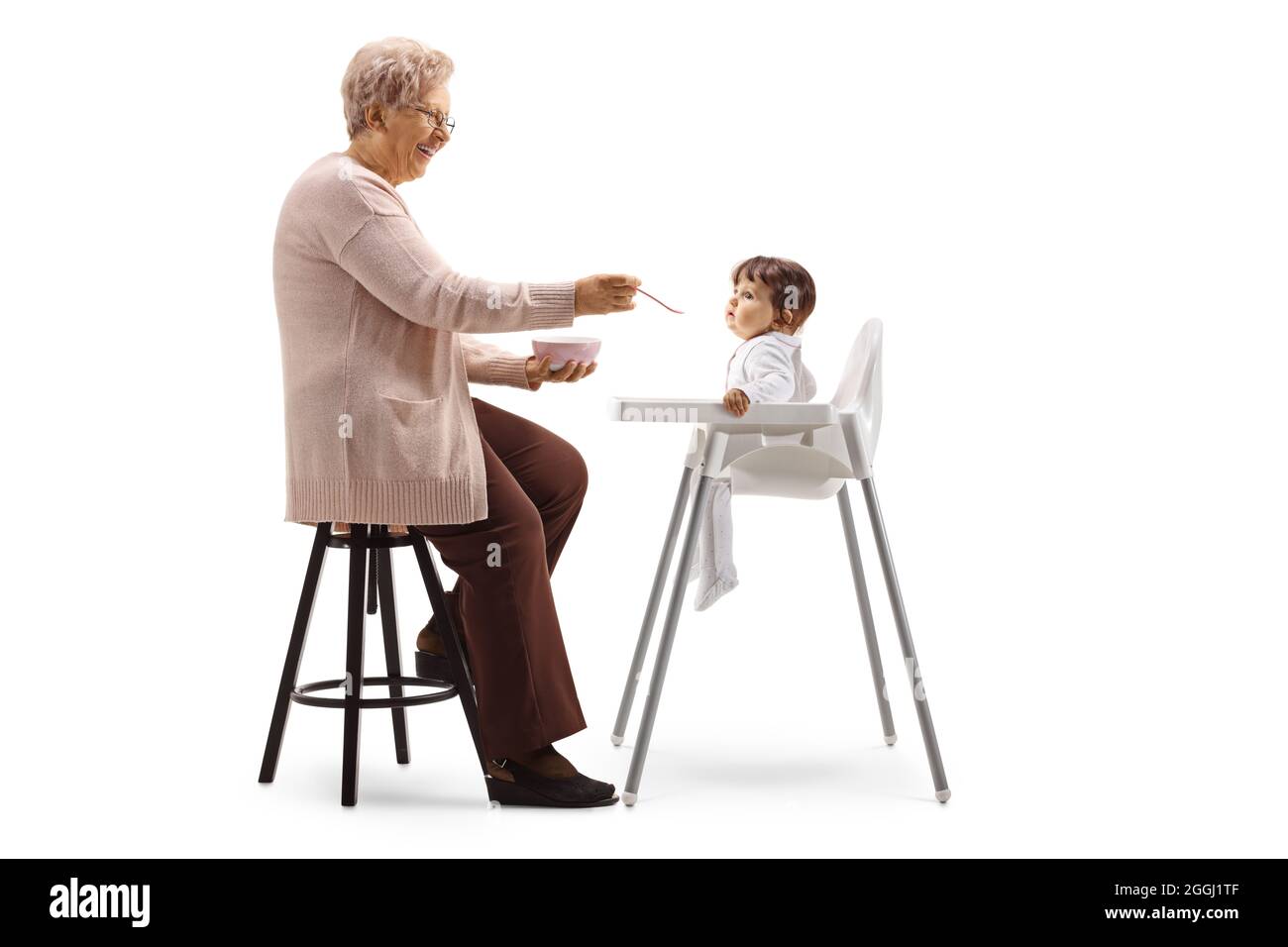 Oma füttert ein Baby in einem Stuhl isoliert auf weißem Hintergrund Stockfoto