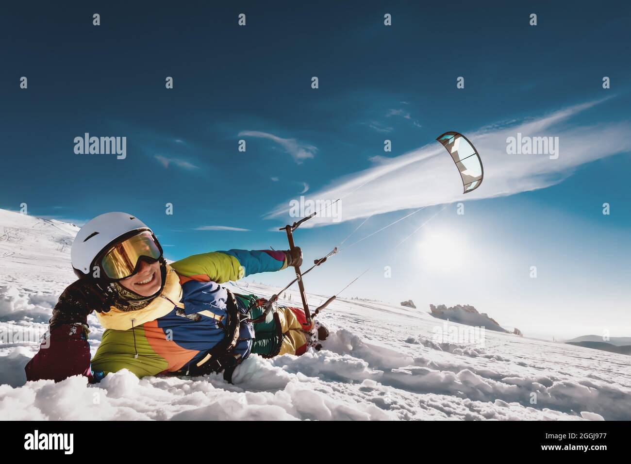 Erwachsene Kite Surfer liegt auf dem Schnee mit Drachen in der Hand und lächeln. Snowkiten Konzept mit Ski oder Snowboard Stockfoto