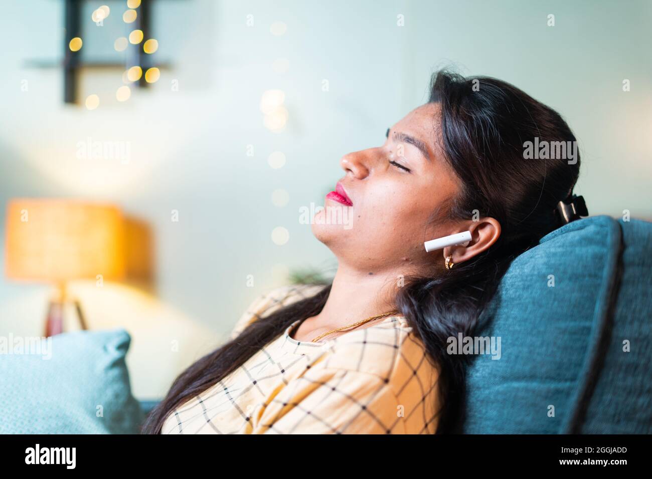 Junges Mädchen mit geschlossenen Augen, das sich auf dem Sofa lehnt und auf dem kabellosen Kopfhörer Lieblingslied im Wohnzimmer hört – Konzept der Pause Stockfoto