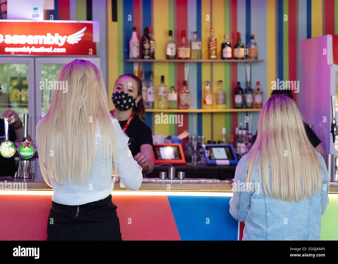 Zwei Frauen, die an einer Bar Alkoholgetränke kaufen, Rückansicht von 2 blonden Frauen, im Edinburgh Fringe, Edinburgh, Schottland, Großbritannien Stockfoto