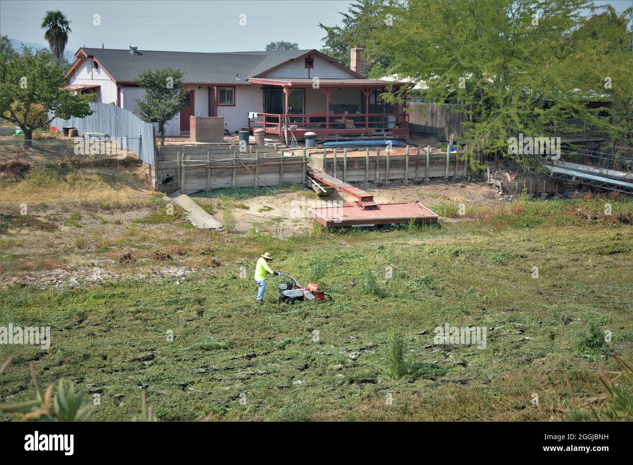 Mann, der Unkraut in einem trockenen, getrockneten Kanal hinter seinem Haus schneidet ein Dock nach 8-jähriger Dürre im nördlichen Kalifornien hat kein Wasser für den Zugang zu Booten Stockfoto