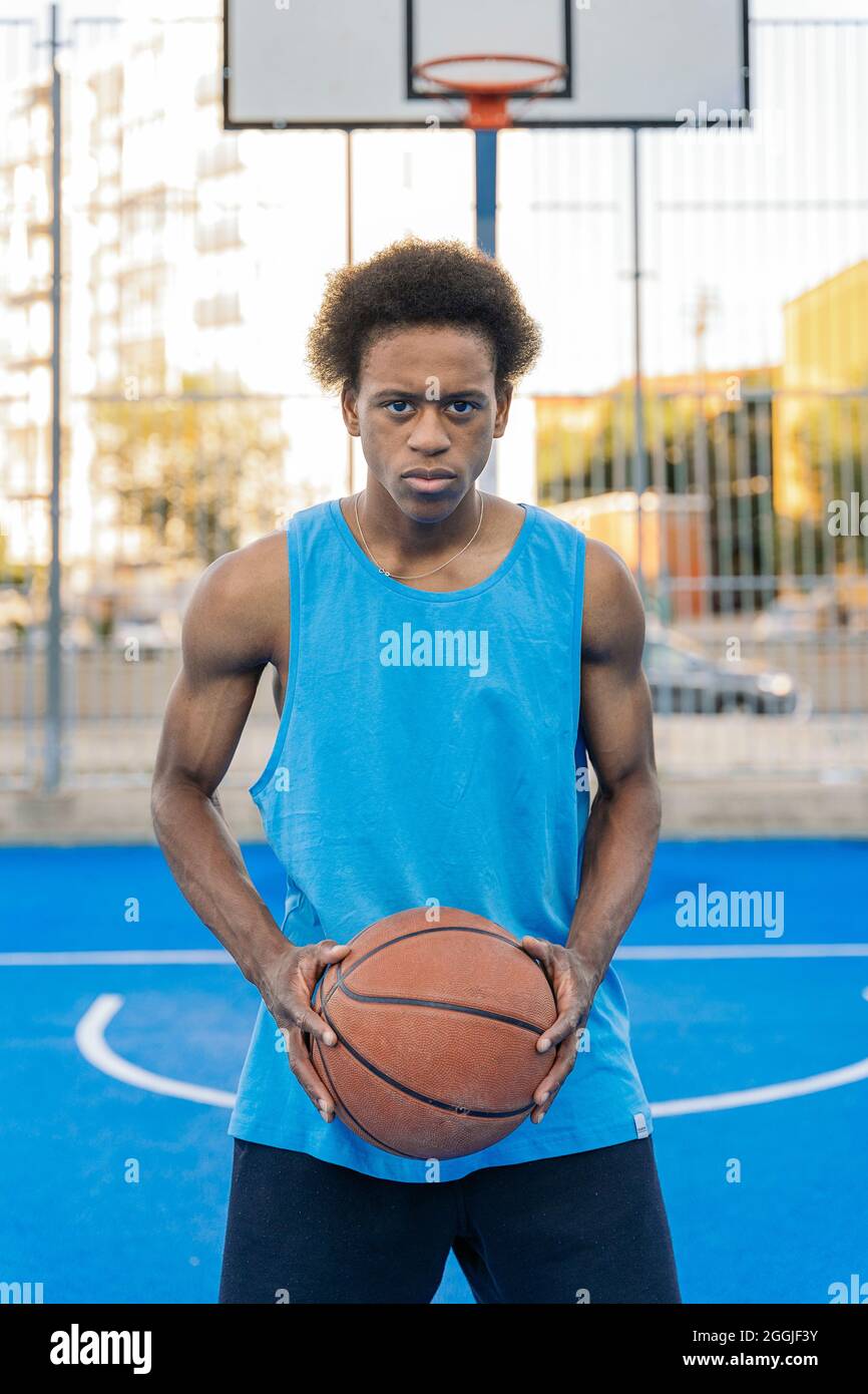 Konzentrierter afro-amerikanischer Basketballspieler, der die Kamera anschaut, die den Ball mit seinen Händen in einem Straßenbasketballfeld hält. Stockfoto