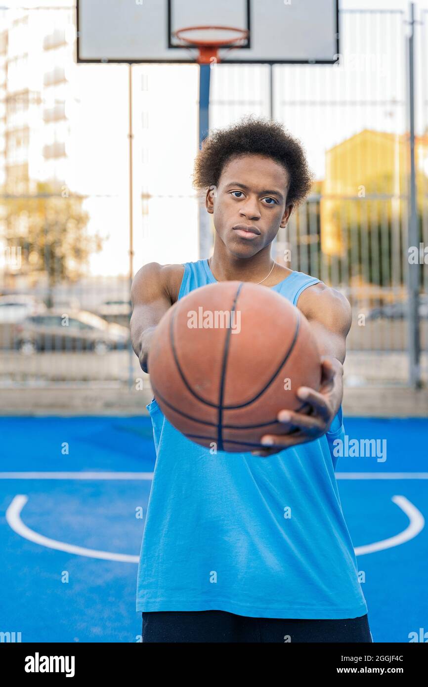 Konzentrierter afro-amerikanischer Basketballspieler, der die Kamera anschaut, die den Ball mit seinen Händen in einem Straßenbasketballfeld hält. Stockfoto
