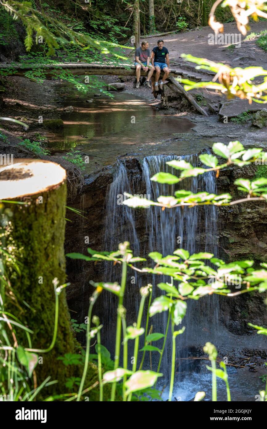 Europa, Deutschland, Baden-Württemberg, Schwäbischer Wald, Murrhardt, Zwei Männer sitzen auf der Holzbrücke über den vorderen Hörschbach-Wasserfall Stockfoto