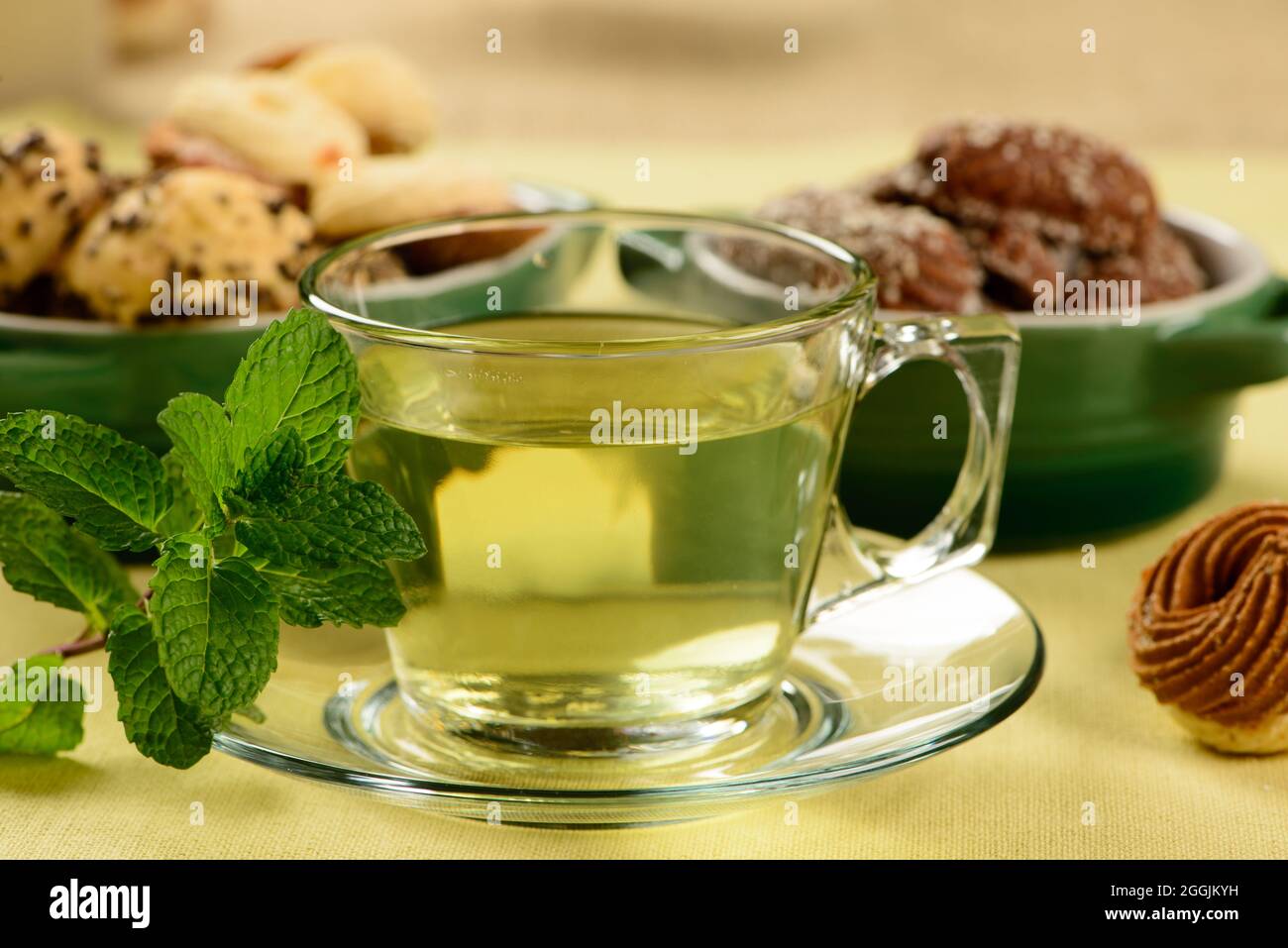Minztee in transparenter Tasse mit süßen Plätzchen um Stockfoto