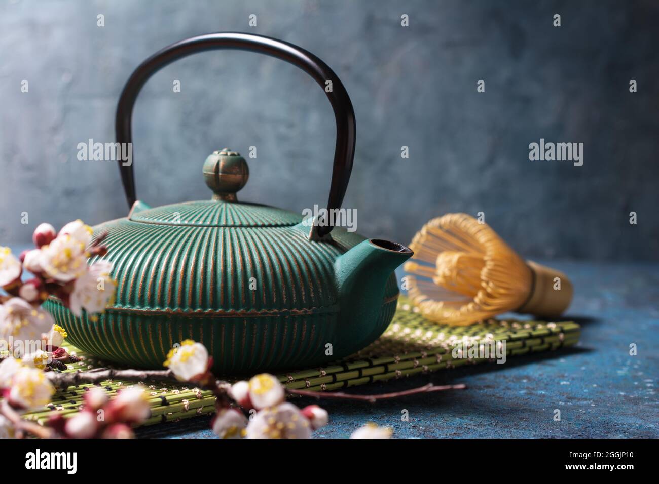 Schöne Frühlingskomposition mit traditionellem türkis-asiatischem Gusseisen-Kessel, Bambusbesen oder -Chasen und blühenden Aprikosenzweigen auf Blau Stockfoto