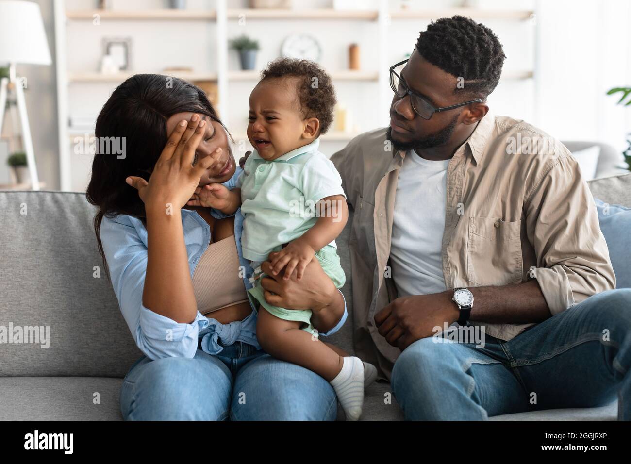 Müde afroamerikanische Eltern sitzen mit weinenden Kind auf dem Sofa Stockfoto