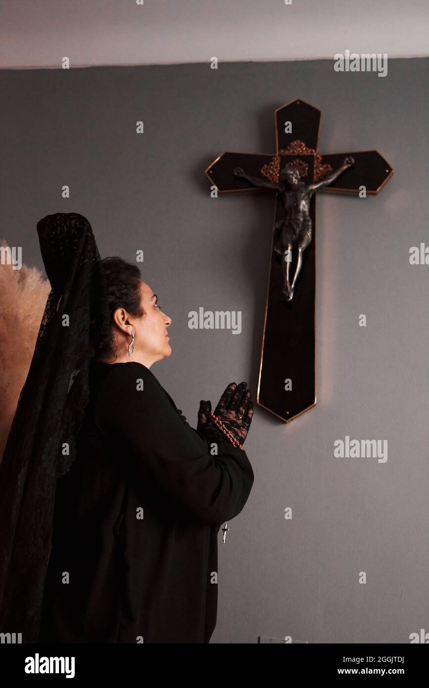 Eine Frau mit einem schwarzen Schleier, die vor einem Kruzifix betet Stockfoto