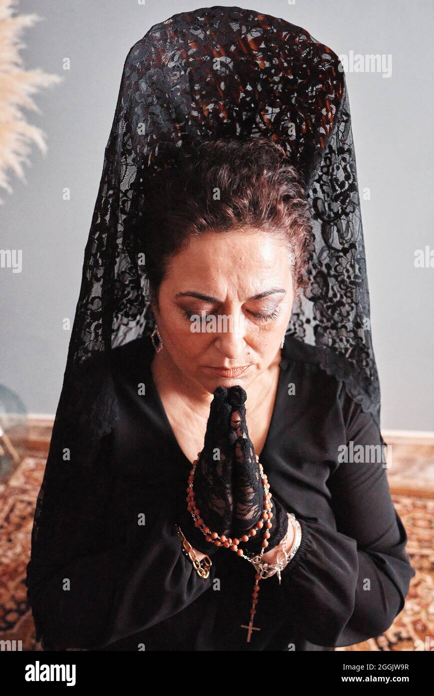 Eine Frau mit einem hohen Kamm und einem schwarzen Schleier, die betet Stockfoto