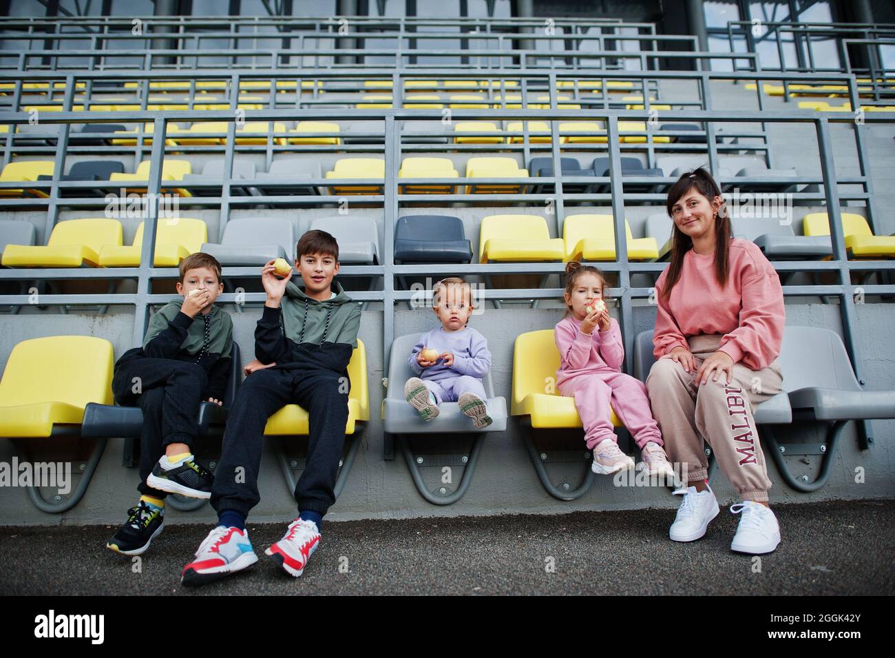 Junge, stilvolle Mutter mit vier Kindern, die auf Stühlen im Stadion sitzen. Familie verbringt Freizeit im Freien. Stockfoto