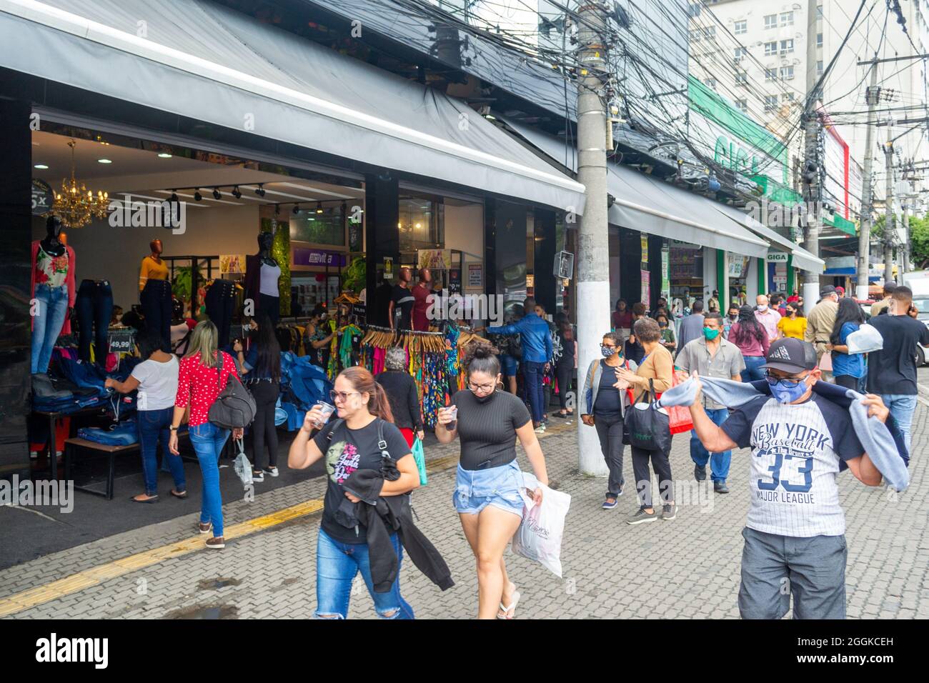 Brasilianische Menschen tragen schützende Gesichtsmasken wie der Spaziergang im Marktviertel in Niteroi, Rio de Janeiro, Brasilien. Ein Geschäft ist in der zu sehen Stockfoto