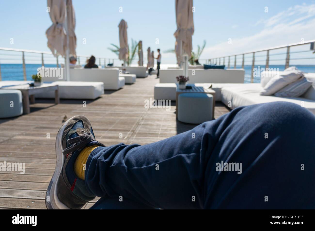 Ein Mann mit gekreuzten Beinen, der in einer Lounge-Bar am Meer die Sonne genießt Stockfoto