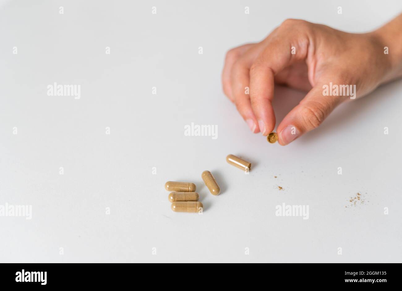 Nahaufnahme der Hand mit Kräuterkapsel auf weißem Hintergrund. Mikrodosierkonzept. Psychedelika-Therapie. Depression, Angstbehandlung Stockfoto