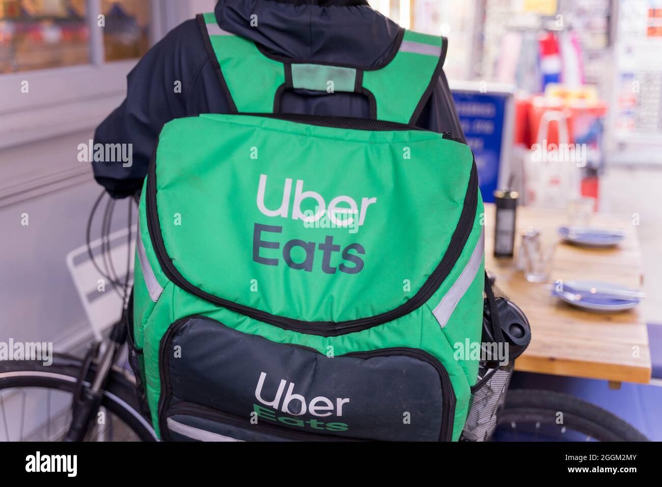 Lebensmittelzustellung UBBER frisst Fahrer mit grünem Hintersack Stockfoto