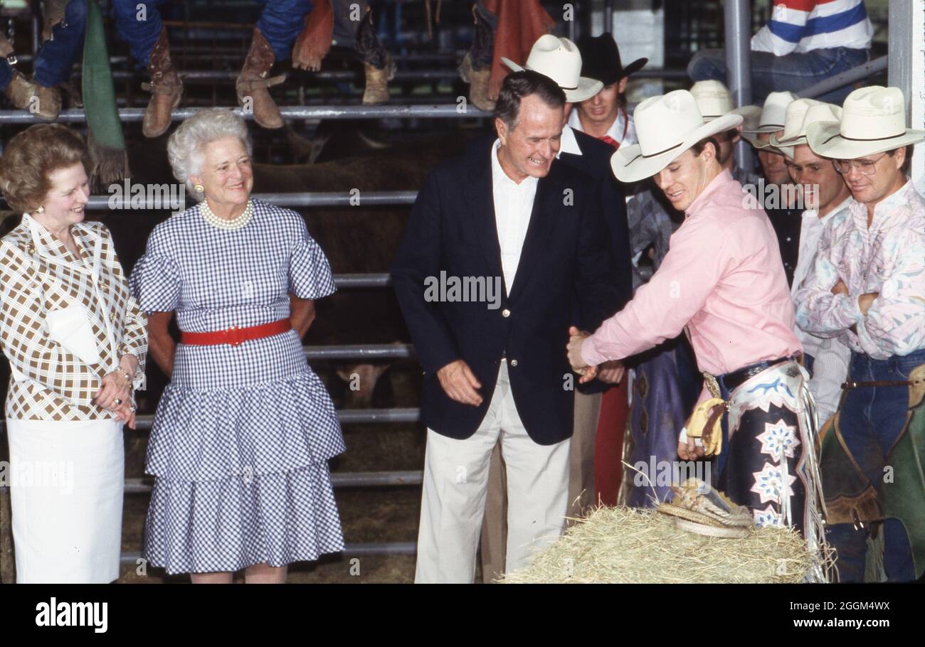 Houston Texas USA, 12. Juli 1990: US-Präsident George H.W. Bush schüttelt sich die Hände mit einem Cowboy bei einem texanischen Rodeo, das für die Teilnehmer des Wirtschaftsgipfels der Industrienationen mit Weltführern veranstaltet wird. Die britische Premierministerin Margaret Thatcher steht links und First Lady Barbara Bush ist in der Mitte. ©Bob Daemmrich Stockfoto