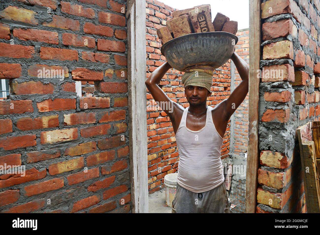 Arbeiter, die Ziegelsteine auf dem Kopf auf der Baustelle tragen Stockfoto