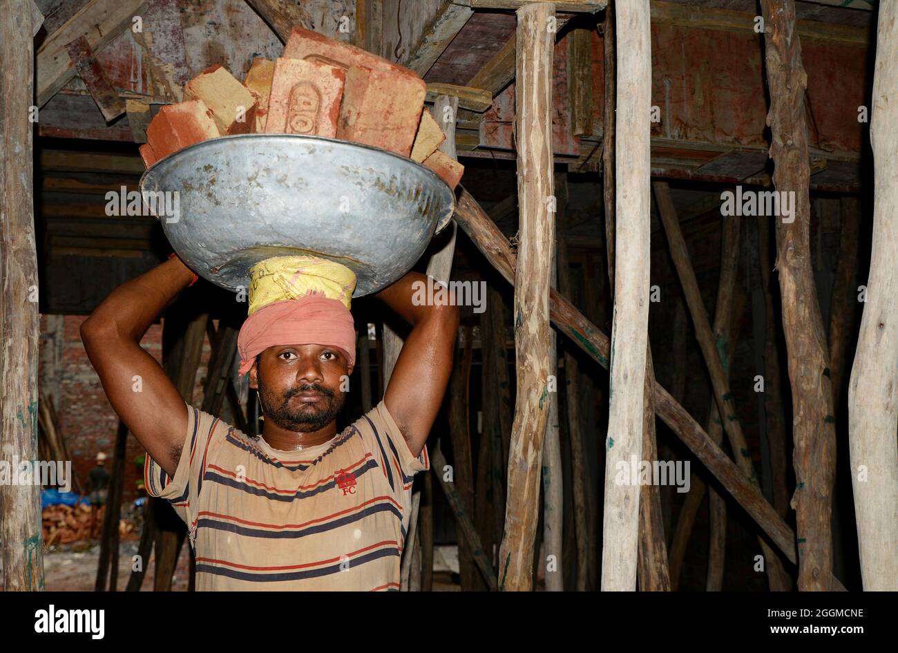 Arbeiter, die Ziegelsteine auf dem Kopf auf der Baustelle tragen Stockfoto