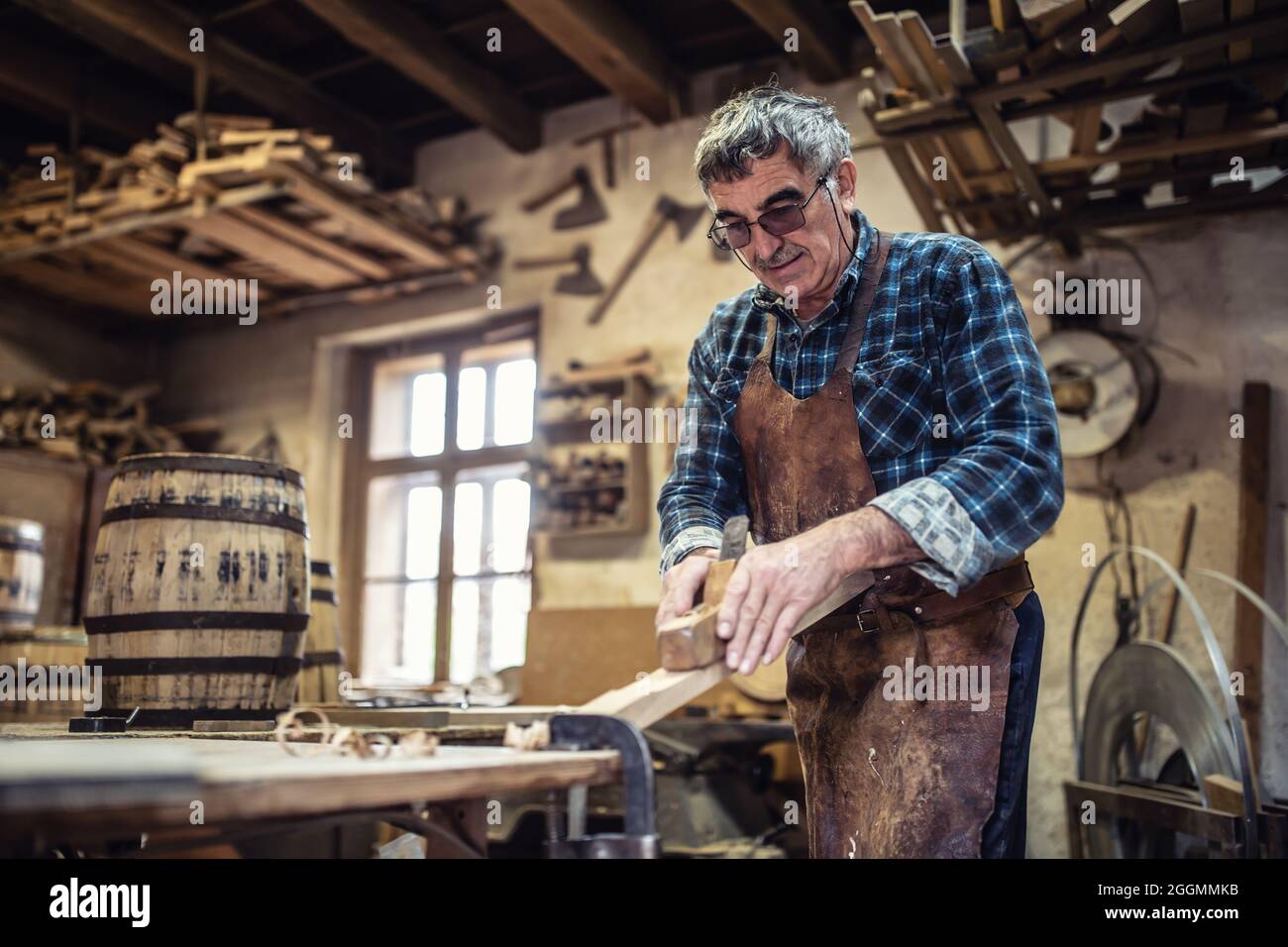 Zimmermann in Gläsern verwendet Wagenheber, um die Oberfläche des Holzes in der Werkstatt zu glätten. Stockfoto