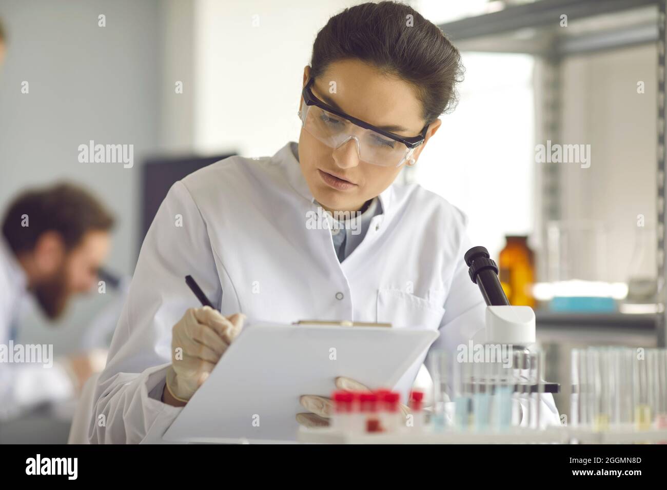 Wissenschaftler, die sich Notizen machen, während sie medizinische Forschung im modernen wissenschaftlichen Labor betreiben Stockfoto