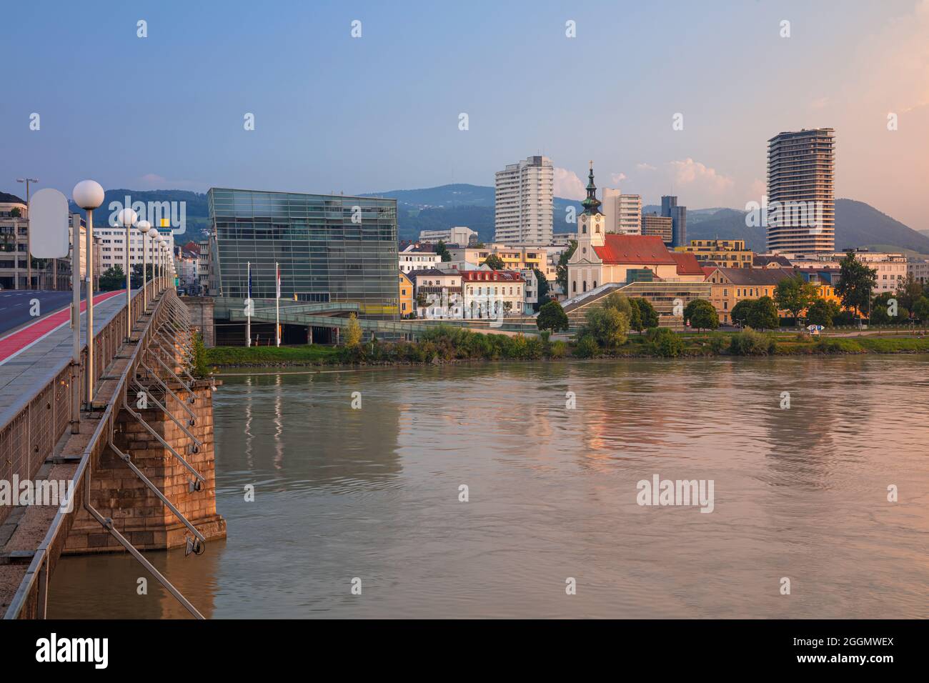 Linz, Österreich. Stadtbild des Flussufers Linz, Österreich bei Sonnenaufgang im Sommer mit Spiegelung der Lichter der Stadt in der Donau. Stockfoto