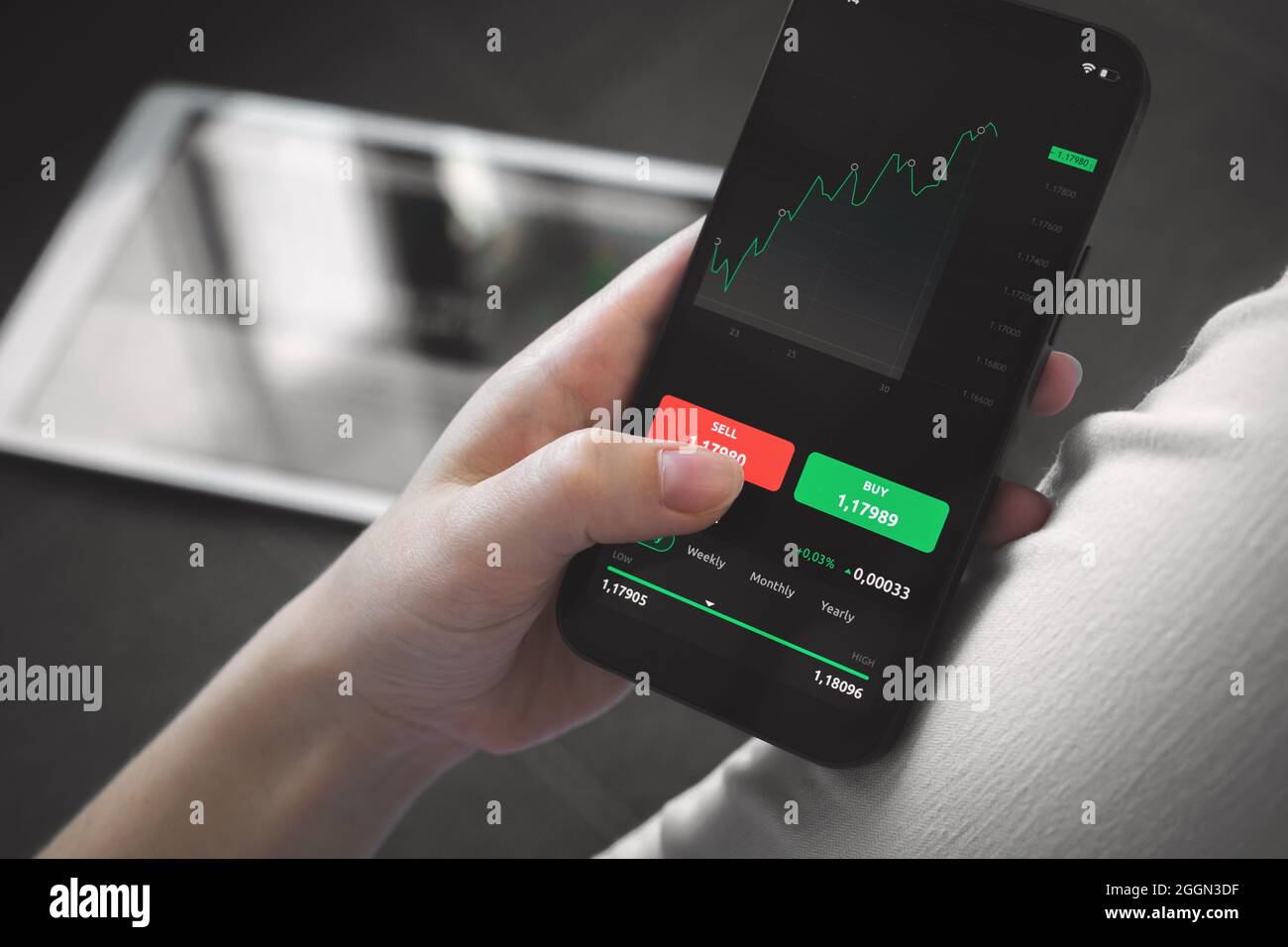 Börsenhandel zu Hause. Person, die Mobiltelefon mit Finanzgraphen für Investitionen, Kauf und Verkauf verwendet Stockfoto
