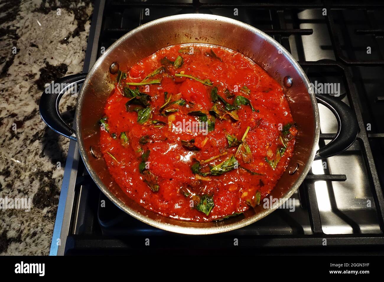 Nudelsauce mit roten Tomaten, mit etwas grünem Kraut auf der Oberseite, kocht in einem Topf auf einem Herd. Stockfoto