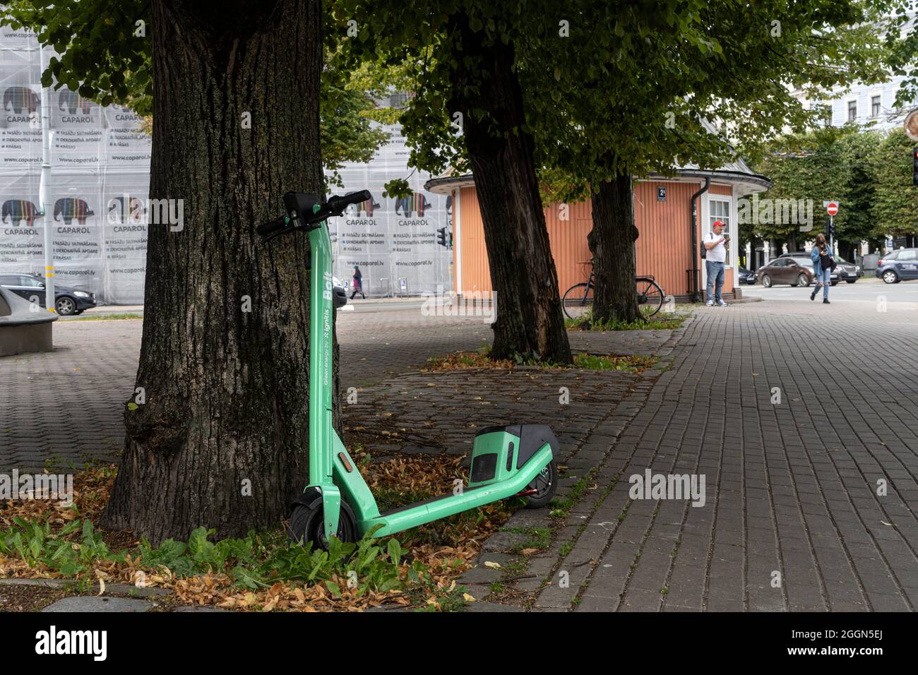 Riga, Lettland. 2021. August. Ein Elektroroller, der sich auf dem Bürgersteig einer Straße im Stadtzentrum an einen Baum lehnt Stockfoto