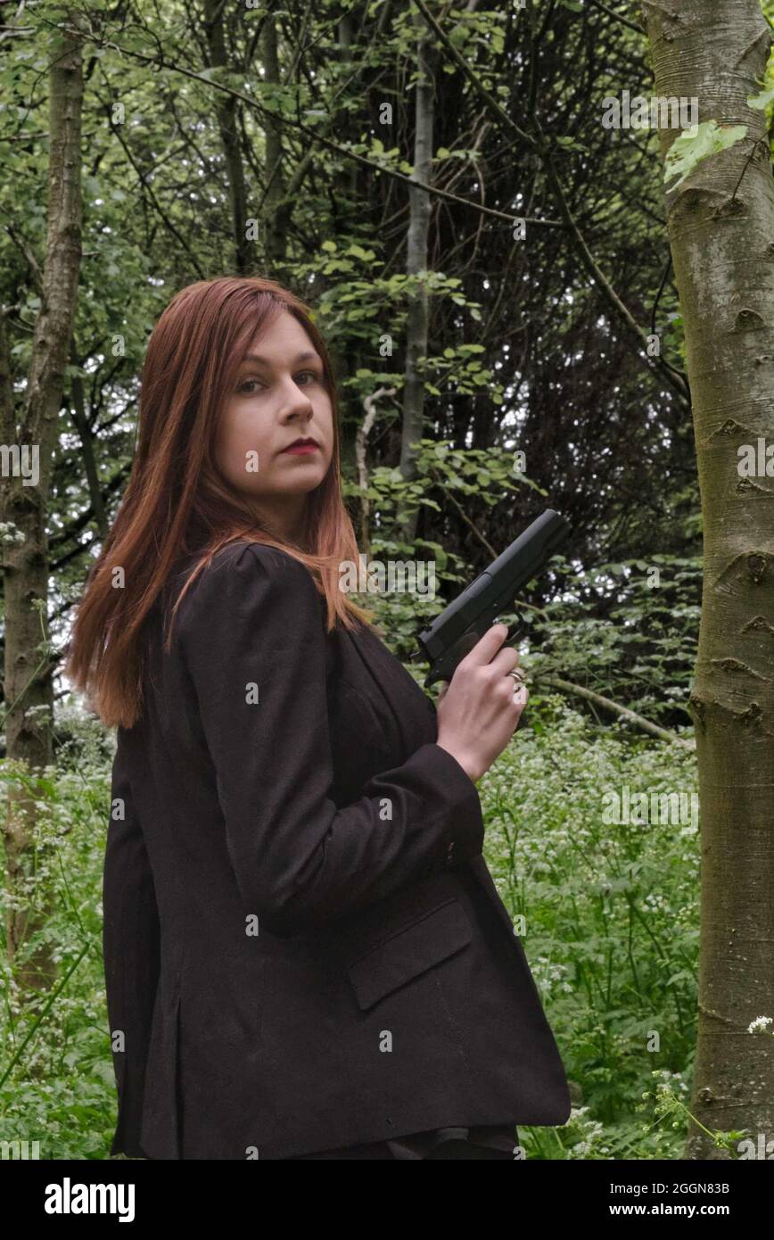 Pistole toting junge Frau im Wald gekleidet in schwarz, weibliche Geheimagentin Stil. Stockfoto