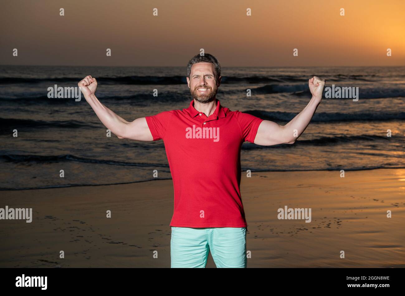 Erfolgreicher Kerl am Strand. kaukasischer Kerl am Sonnenaufgangsstrand. Bärtiger Mann im Hemd. Stockfoto
