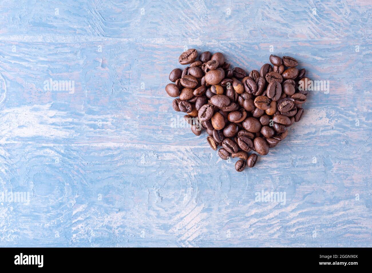 Herzform aus Kaffeebohnen auf blauem stilvollem Holzhintergrund, Nahaufnahme, Draufsicht, Flat Lay, Kopierraum. Symbol der Liebe zum Kaffee Stockfoto