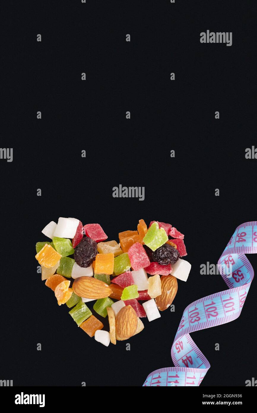 Diät-Food-Konzept für Valentinstag. Schlankheitskonzept. Herzförmige getrocknete Früchte und Nüsse und Maßband isoliert auf schwarzem Hintergrund, Kopie SPAC Stockfoto