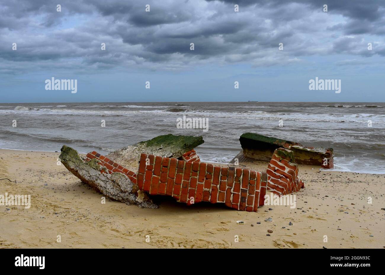 Zerstörte Ziegelmauer, die am Strand liegt und vom Meer aufgrund der Klimakrise der Küstenerosion gewaschen wurde Stockfoto