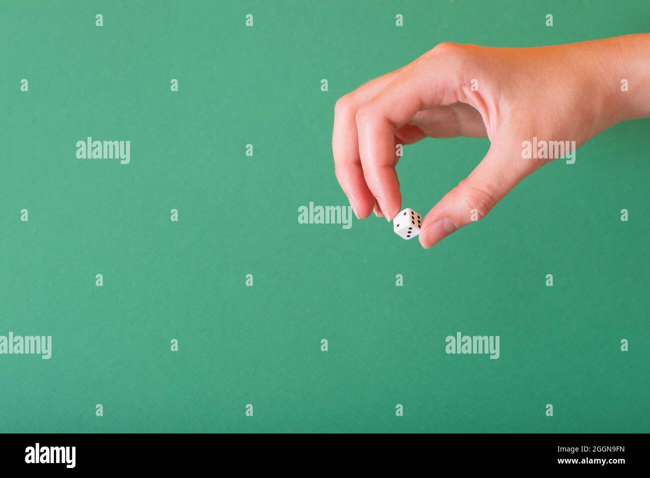 Die weibliche Hand hält einen weißen Würfel auf einem grünen Hintergrund. Idee für Glücksspiel, Casino, Würfelspiele. Stockfoto