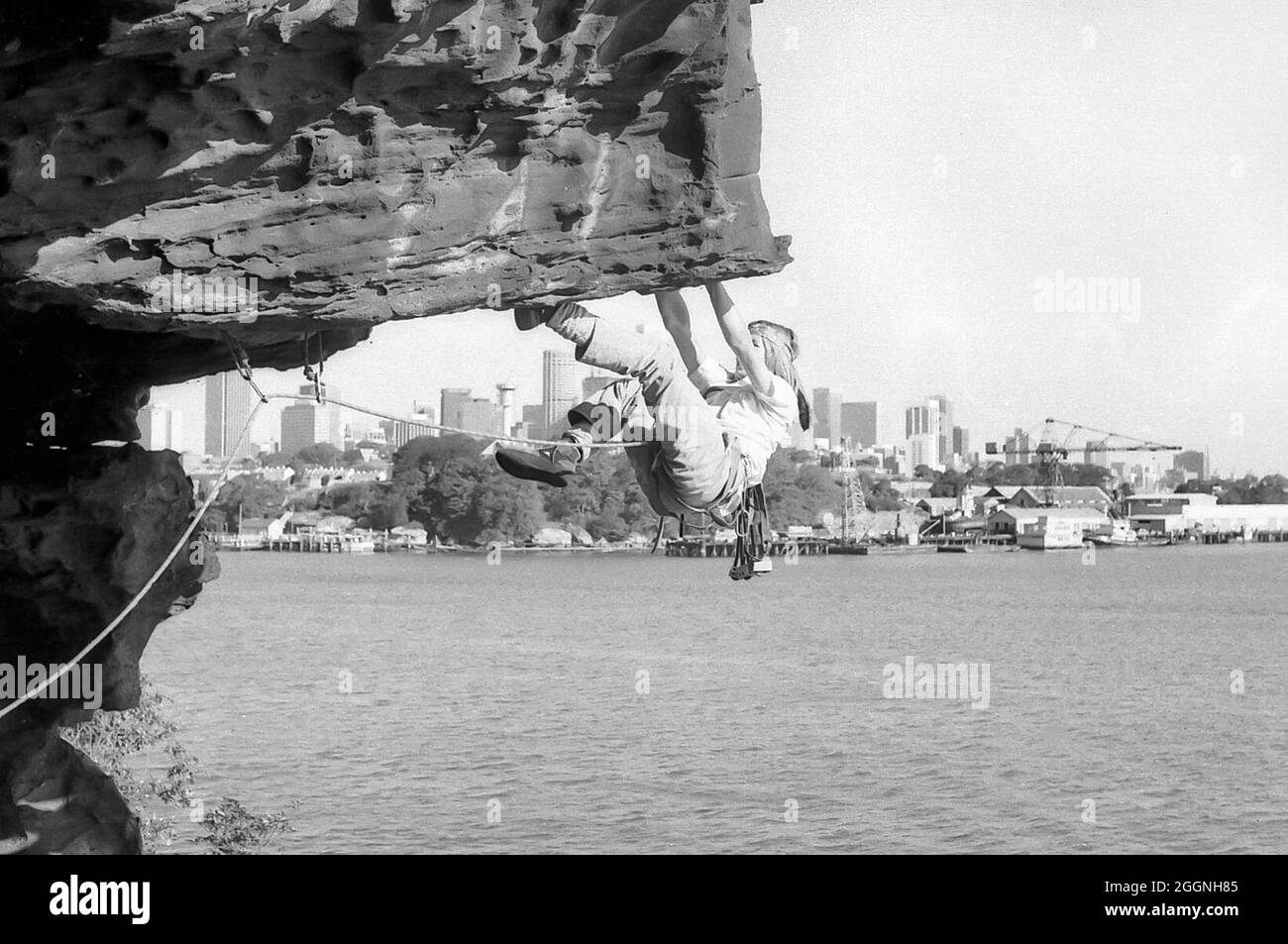 Ein Bild aus dem Jahr 1978 von einem Studenten aus dem Jahr 12, Warwick Baird, der eine Steigung am Balls Head Reserve bestieg, mit Goat Island und der Innenstadt von Sydney im Hintergrund. Beachten Sie die nicht überlaufene Skyline der Stadt im Vergleich zu heute. Klettern jeglicher Art innerhalb des Reservats ist seit 1996 verboten Stockfoto