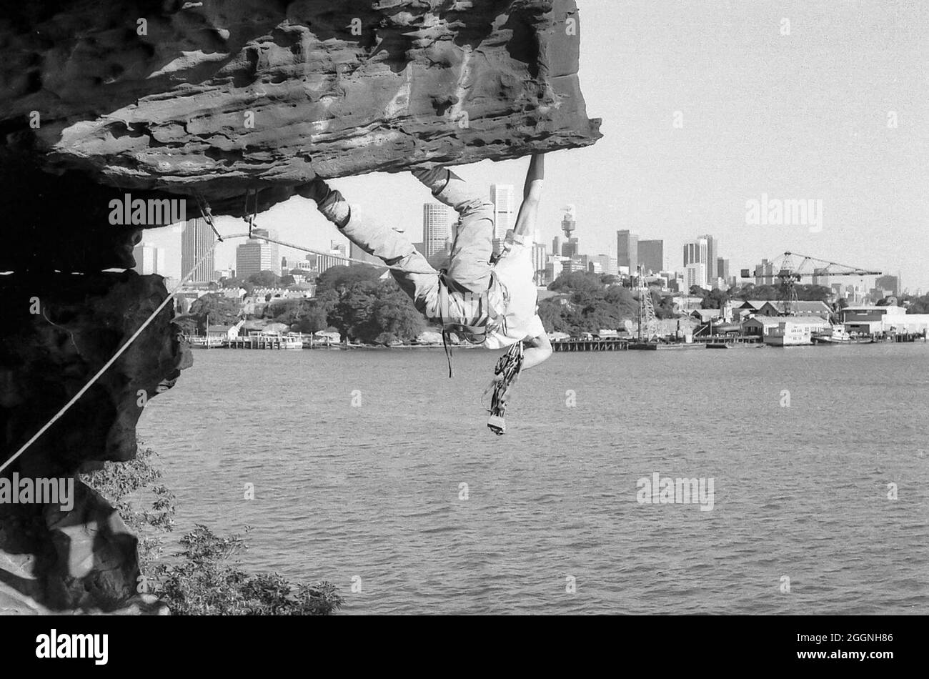 Ein Bild aus dem Jahr 1978 von einem Studenten aus dem Jahr 12, Warwick Baird, der eine Steigung am Balls Head Reserve bestieg, mit Goat Island und der Innenstadt von Sydney im Hintergrund. Beachten Sie einen unvollendeten Mittelpunkt (Sydney Tower). Klettern jeglicher Art innerhalb des Reservats ist seit 1996 verboten Stockfoto