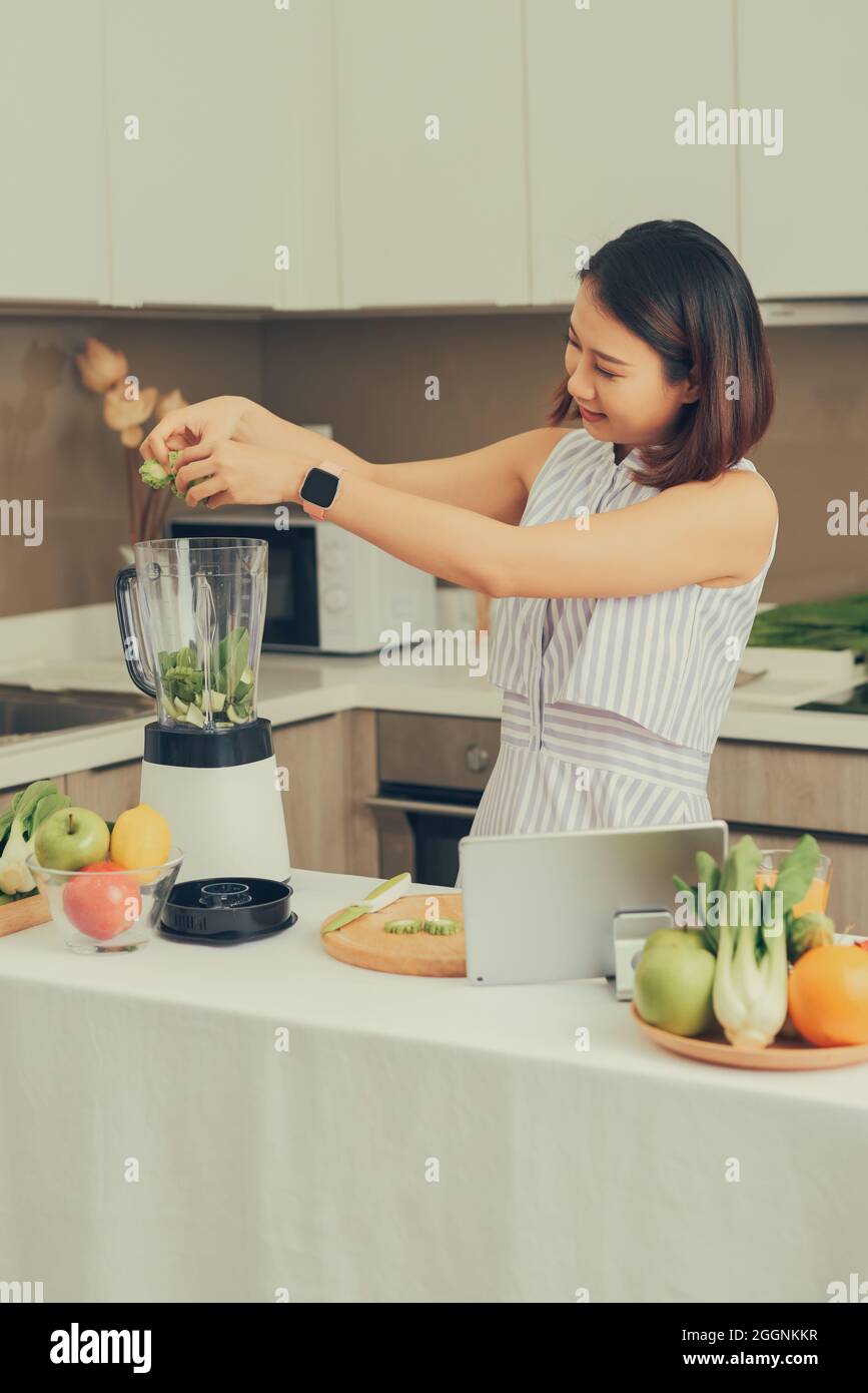 Lächelnd vegane asiatische Frau einen Smoothie mit Obst und Gemüse in der Küche Stockfoto