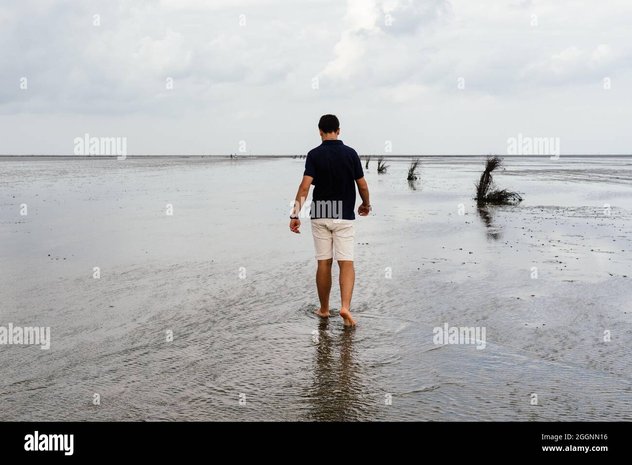 Junger erwachsener Mann, der bei Ebbe allein an einem ruhigen und ruhigen Strand im Wattenmeer, Deutschland, läuft. Blick von hinten Stockfoto