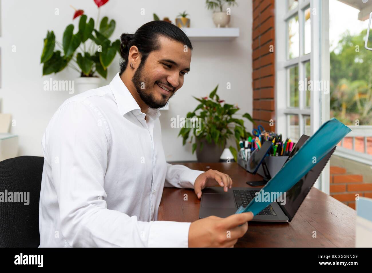 Junger Latino-Mann mit Ordner, der in einem Laptop arbeitet Stockfoto