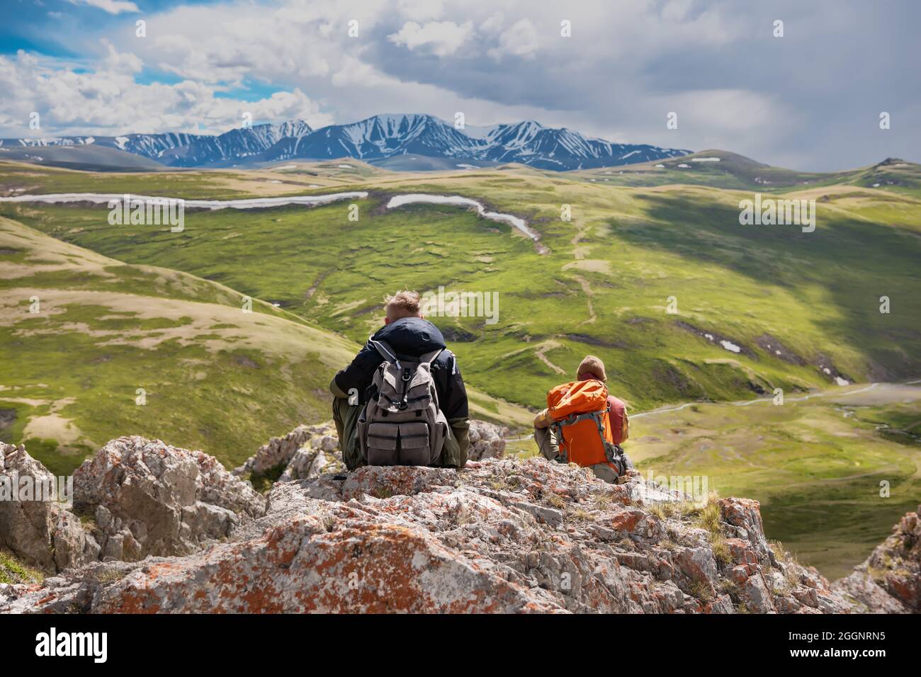 Zwei Rucksacktouristen oder Reisende sitzen und ruhen sich auf einem großen Felsen aus und blicken auf die Berge Stockfoto