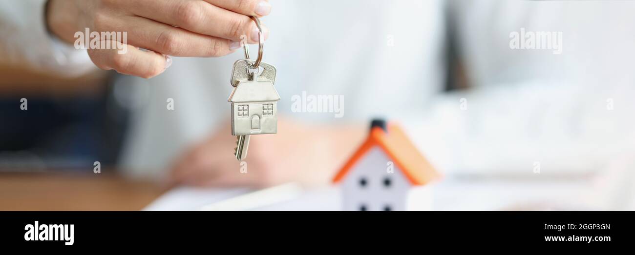 Weibliche Hand, die Schlüssel mit Schlüsselanhänger in der Nähe des Spielzeughauses hält Stockfoto
