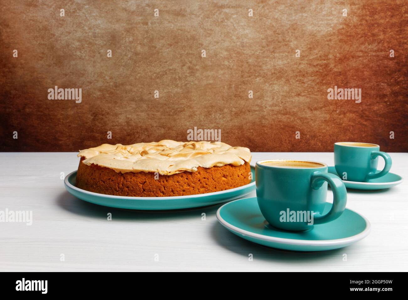 Hausgemachter Beerenkuchen mit Baiser und zwei Tassen Kaffee-Espresso auf weißem Holztisch. Weitwinkelansicht von vorne. Copyspace. Stockfoto