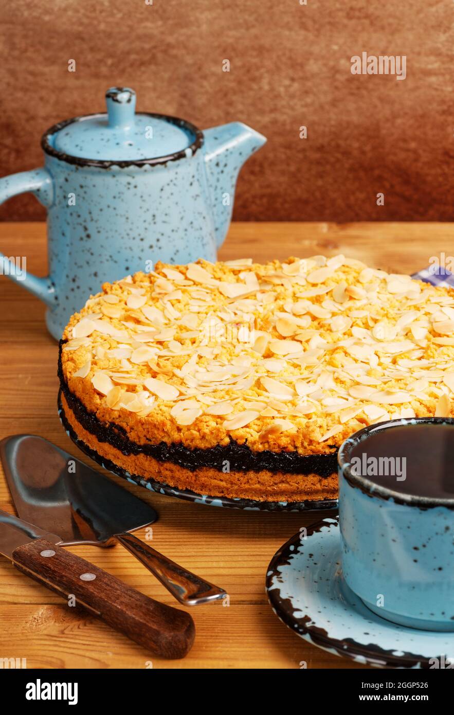 Hausgemachter Kuchen mit schwarzer Johannisbeere, verziert mit Mandelblüten und einer Tasse Tee auf einem Holztisch. Stockfoto