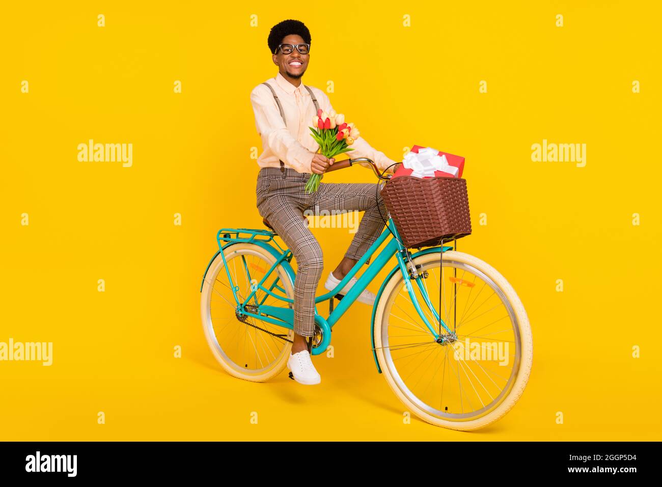 Foto von fröhlich gut gepflegten Kerl fahren Fahrrad halten Blumen tragen Strumpfhalter Hemd isoliert gelbe Farbe Hintergrund. Stockfoto