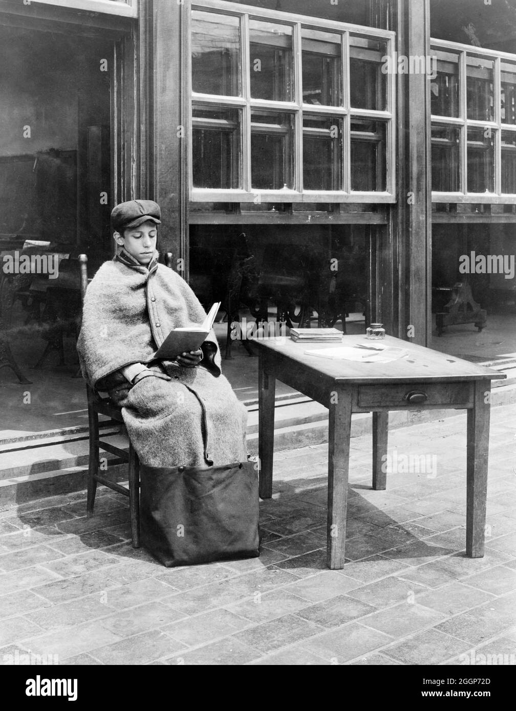 Ein Junge, der eine Sitztasche der Marke Huyck trägt (ein Mantel mit einer Tasche am Boden), um sich in einer Open-Air-Schule in New York, 1918, zur Zeit der Spanischen Grippe-Pandemicirca, die von Jessie Tarbox Beals fotografiert wurde, warm zu halten. Stockfoto