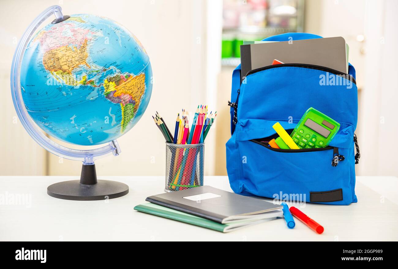 Zurück zur Schule. Studentenrucksack und Zubehör auf weißem Schreibtisch, verwischen den Hintergrund im Innenraum. Bildung, Studienkonzept Stockfoto