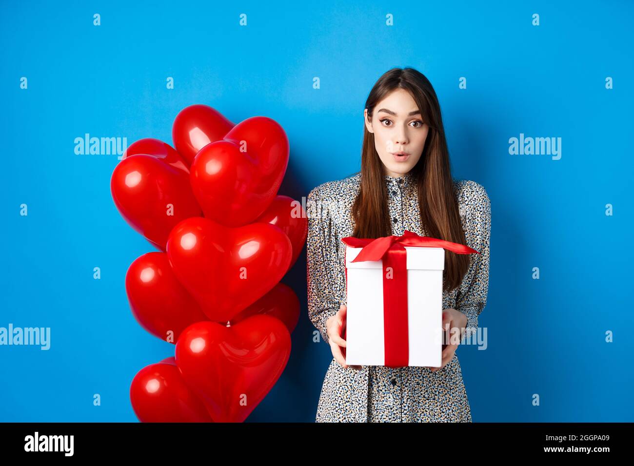 Valentinstag Uberrascht Attraktives Madchen Das An Der Kamera Erstaunt Halt Grosse Romantische Geschenk In Der Nahe Von Roten Herzen Ballons Blauer Hintergrund Stockfotografie Alamy