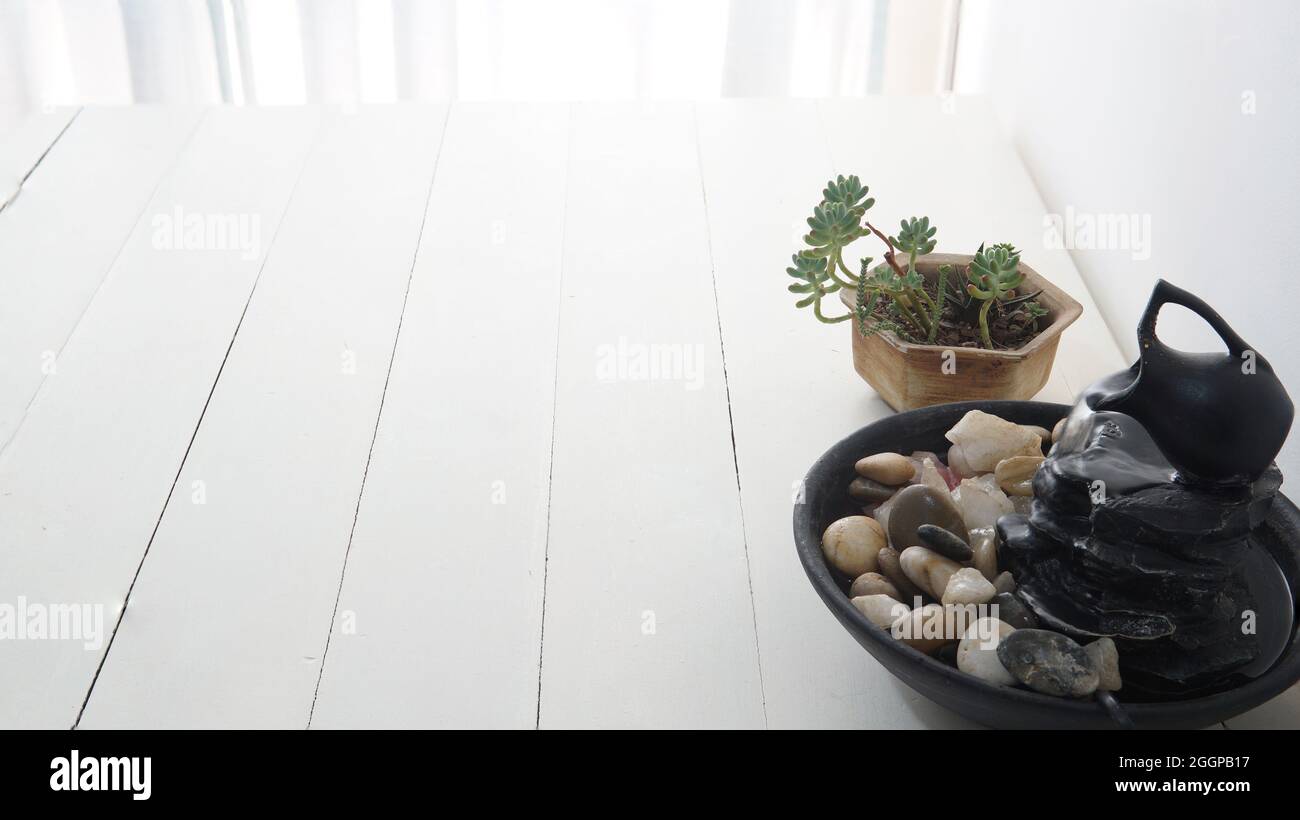 Nahsicht auf einen Zen-Brunnen mit einer kleinen Sukulente dahinter. Platziert auf einem weißen Holztisch Stockfoto